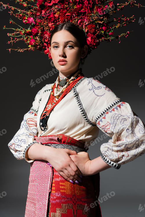 Preview: brunette and pretty ukrainan woman in floral wreath with red berries posing with hand on hip on dark
