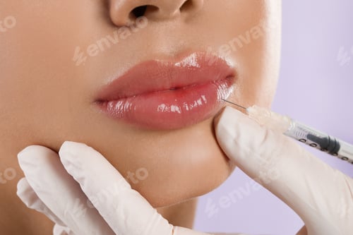 Preview: Young woman getting lips injection on lilac background, closeup