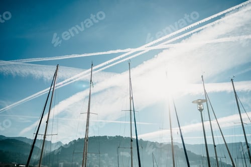 Preview: Low angle shot of boat masts under the sky with jet trials