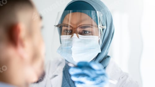 Preview: Islamic Dentist Lady In Hijab And Face Shield Examining Patient's Teeth