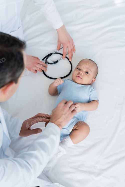 Preview: cropped shot of pediatricians tickling little baby in bed