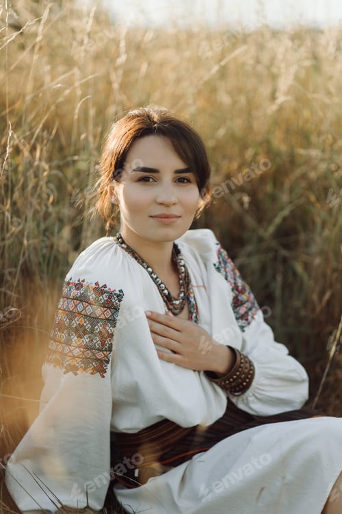 Preview: Young woman in traditional national embroidered shirt and skirt on nature at sunset.