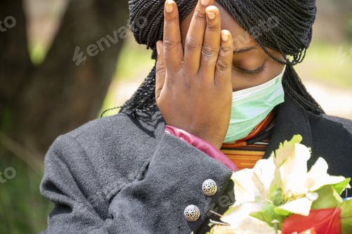 Preview: Shallow focus shot of a young Nigerian woman mourning while holding flowers