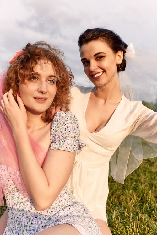Preview: A happy charming bride in a white dress with a white veil and a bridesmaid with a pink veil gently