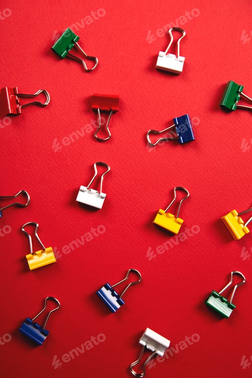 Preview: A lot of colorful paper clips lie on an red background.