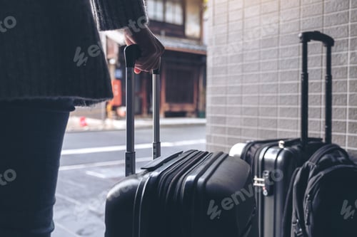 Preview: Closeup image of a woman holding and dragging a black baggage for traveling in the outdoors