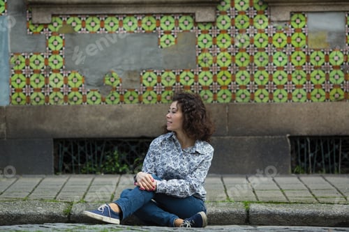 Preview: Mixed-Race Woman Sitting On The Sidewalk In Front Of Houses In Porto, Portugal.