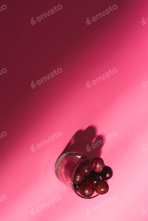 Preview: Close up of glass of red grapes and copy space on pink background
