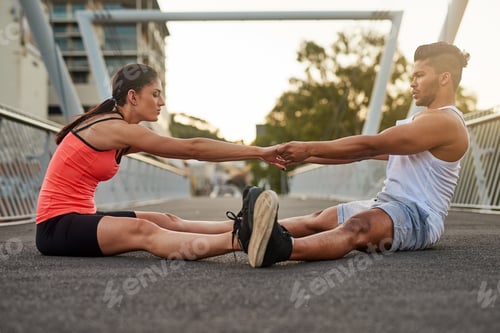Preview: Lemme give you a hand. Shot of a young couple warming up on a bridge before their workout.
