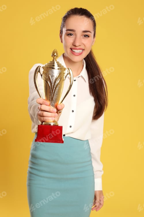Preview: Portrait of happy young businesswoman with gold trophy cup on yellow background