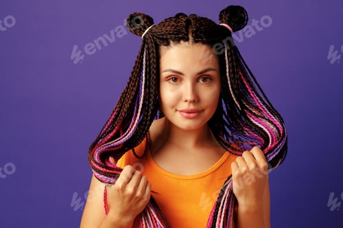 Preview: Smiling positive young woman with colorful african braids on purple background