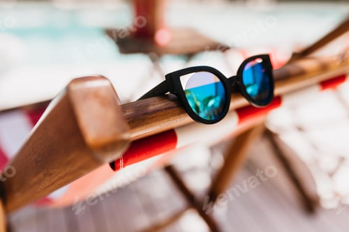 Preview: Blur photo of dark sunglasses. Trendy summer accessory lying on chaise-longue.