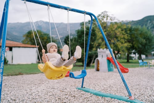 Preview: Little girl swings on a rope swing on a playground in a green park