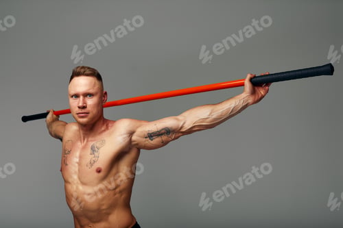 Preview: A fighter shirtless in black shorts, stands in a fighting artificially pose and holds a fight stick