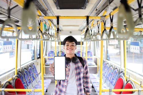 Preview: Young Asian Male Demonstrating Mobile Phone With White Screen For App Design While Standing On Bus