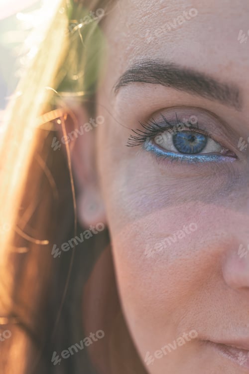 Preview: Portrait of a woman on the beach with blue eyeliner on a blurred background.