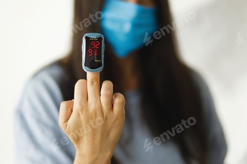Preview: Pulse Oximeter on middle finger, adult female in face mask measuring blood oxygen level