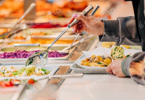 Preview: woman puts food on her plate at the buffet, closeup view