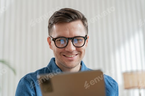 Preview: Close-up of a joyful man with glasses looking over a tablet, bright interior