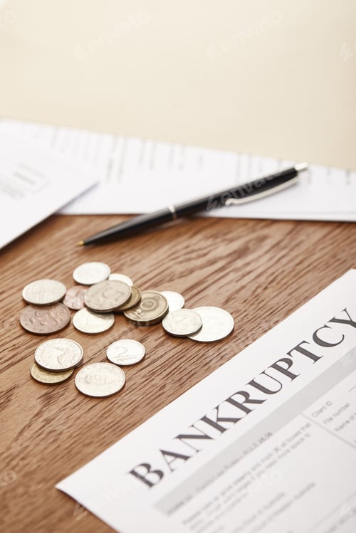 Preview: selective focus of bankruptcy form, pen, coins and documents on brown wooden table