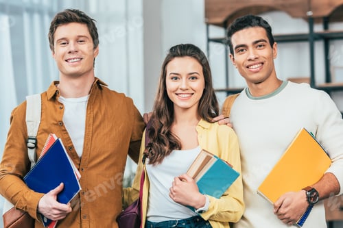 Preview: Three happy multiethnic students holding notebooks and books and looking at camera