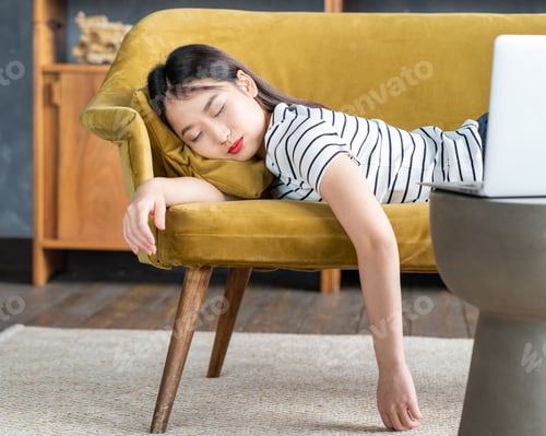 Preview: Young Asian girl fell asleep oncouch in front oflaptop. Cute woman is bored, tired or overworked