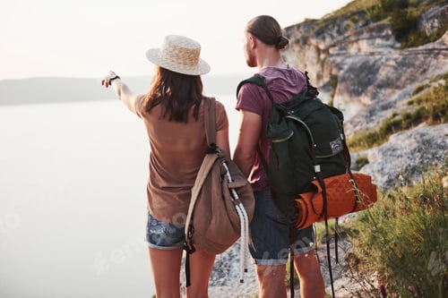 Preview: Two tourist male and woman with backpacks stand to the top of the crag and enjoying sunrise