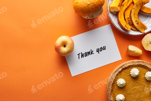 Preview: top view of pumpkin pie, ripe apples and thank you card on orange background