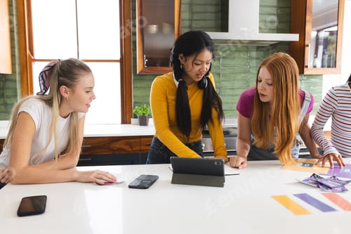 Preview: Teen girls collaborating on school project using tablet in modern kitchen