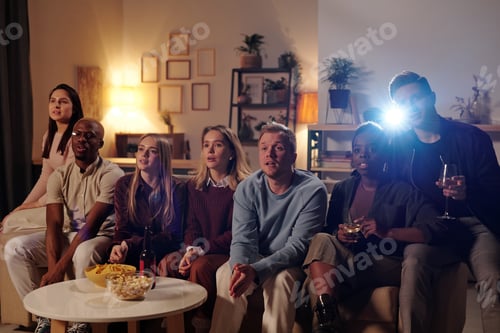 Preview: Group of young intercultural friends sitting on long couch and watching movie