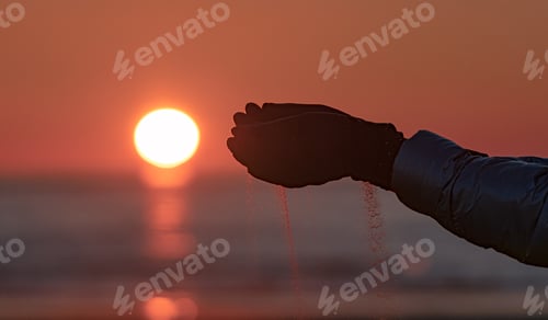 Preview: Closeup of a hand full of sand with the Sun behind at sunset.