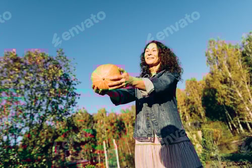 Preview: Joyful woman tossing a pumpkin on a sunny autumn day in the countryside