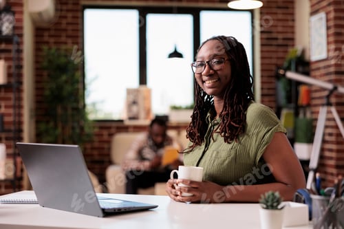 Preview: Portrait of student smiling at camera while holding a cup of coffee or tea sitting at desk with