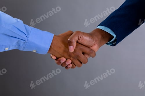 Preview: Mid section of two businessmen shaking hands against grey background