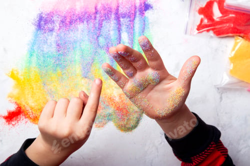 Preview: Child hand painting with rainbow colored sand. Touch of colors creating an abstract rainbow