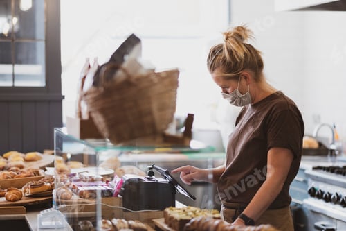 Preview: Blond waitress wearing face mask working in a cafe.