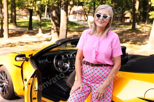 Preview: Stylish senior woman in sunglasses near modern cabriolet outdoors