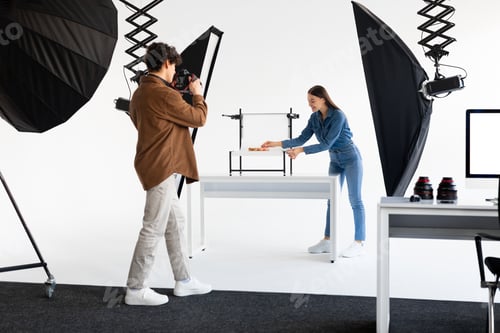 Preview: Young male photographer with photocamera taking photos of composition on white platform while his
