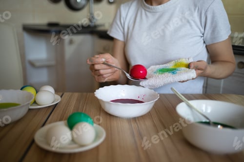 Preview: young beautiful woman in bunny ears paints eggs for easter in the kitchen