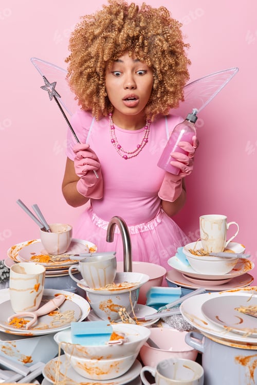 Preview: Shocked cleaning lady wears fairy costume and protective rubber gloves stands near sink with dirty