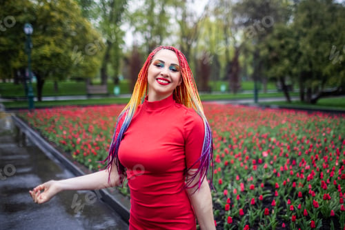 Preview: Cute girl with multi-colored African braids and bright expressive makeup in a tight red dress is