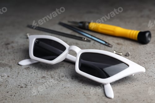 Preview: Stylish female sunglasses and fixing tools on grey table