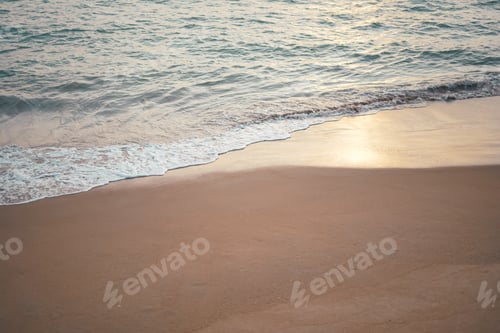 Preview: Ocean wave on sandy beach in twilight time background with sunlight reflection on wet sand.