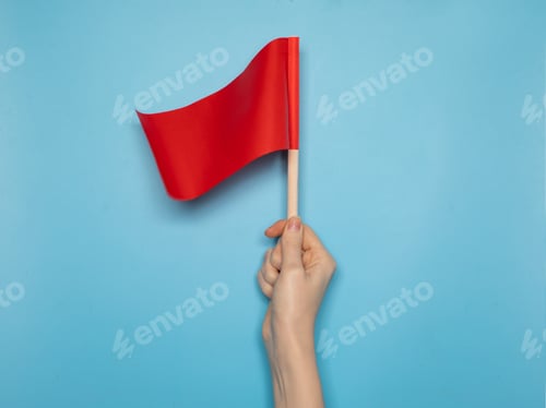 Preview: Hand holding a small red flag against a blue background