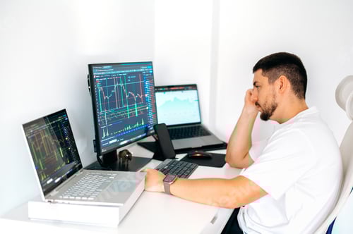 Preview: Focused male trader sitting at home at his work desk, trading on the stock exchange, analyzing the