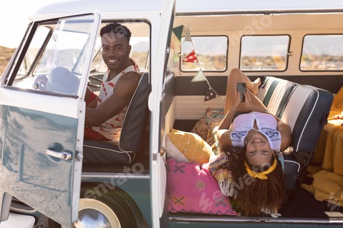 Preview: Side view of happy African-american couple looking at camera in camper van at beach