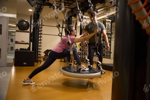 Visualização: Jovem treinador masculino ensinando mulher madura fazendo exercícios esportivos no tapete suspenso