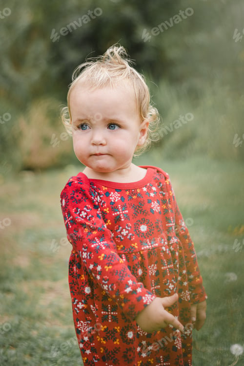 Preview: Cute little toddler girl in red dress outdoors with serious facial expression