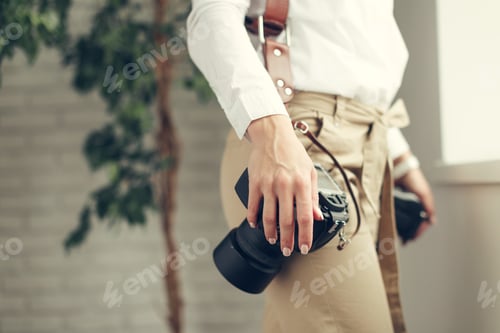 Preview: Woman holding a camera in a casual setting indoors with a plant in the background