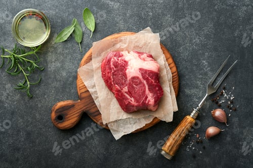 Vista previa: Raw beef steak. Raw fresh Chuck roll steak with rosemary, salt and pepper on cutting board on dark c